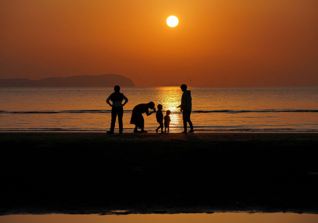 夕暮れの海辺を仲良く歩く家族のシルエット